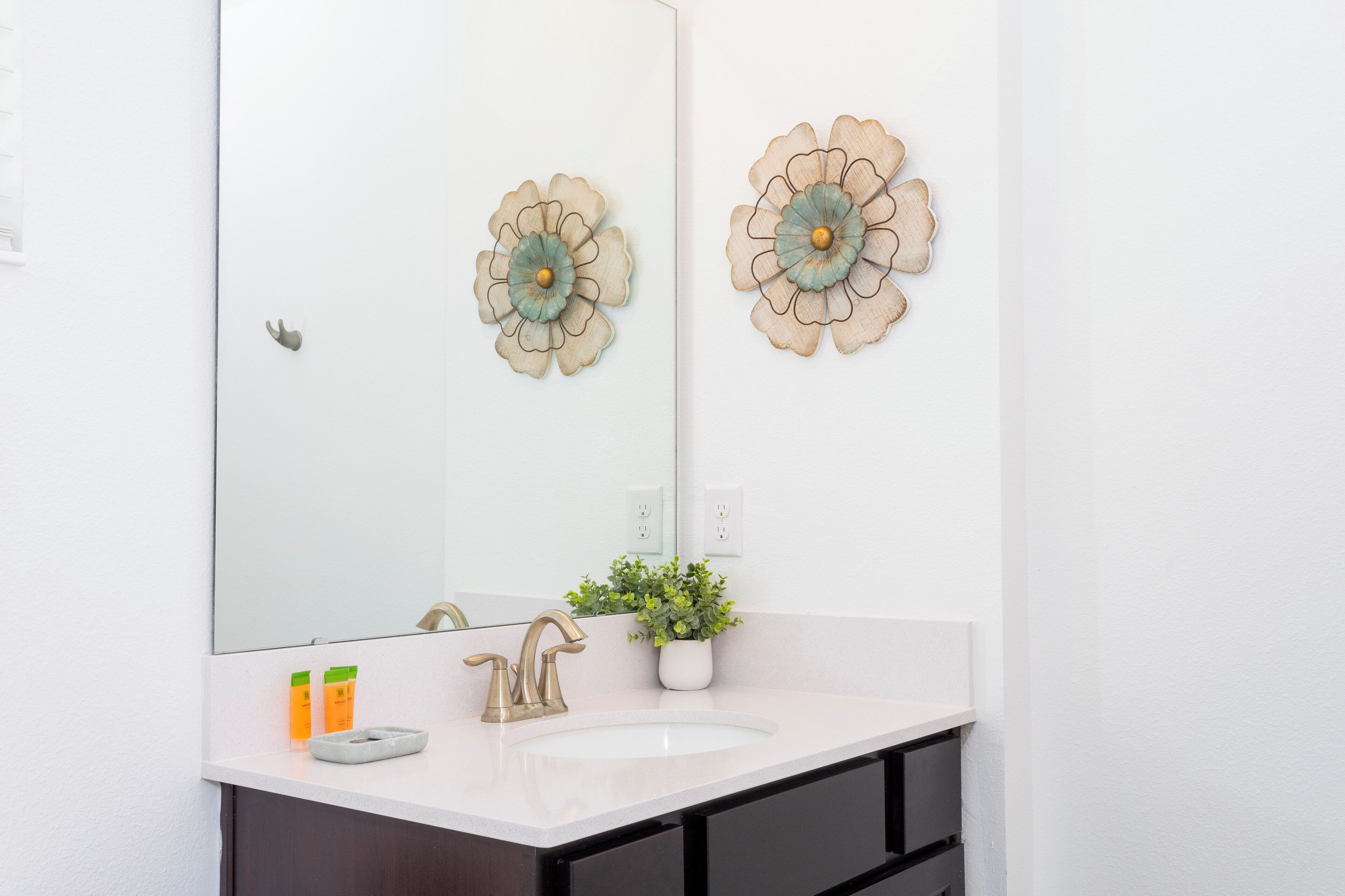 A bathroom with a white sink, a mirror, and two decorative wall flowers.