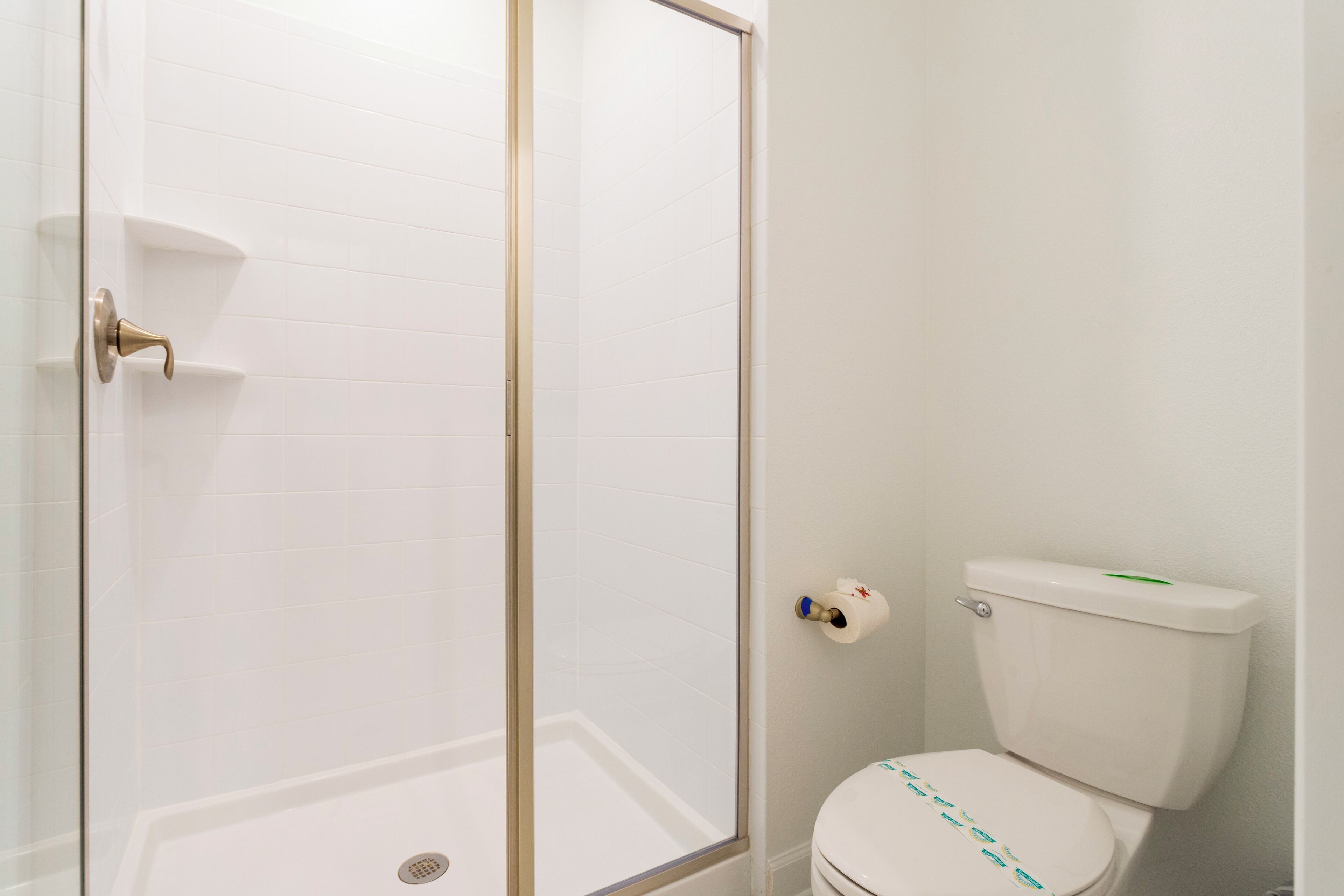 Un baño con cabina de ducha de vidrio, inodoro y pared revestida de azulejos blancos.