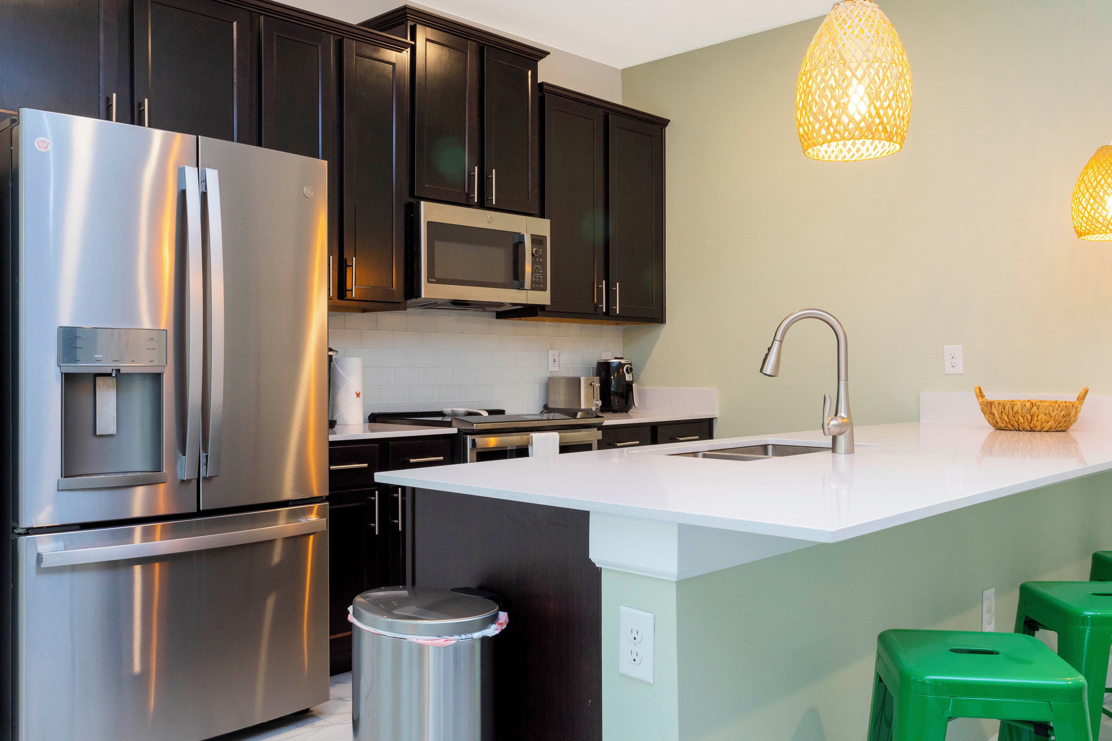 A modern kitchen with dark cabinets, stainless steel appliances, a white countertop island, and green bar stools.