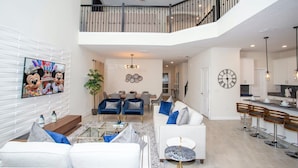 A spacious living area with a high ceiling, a staircase to an upper level, a dining area, and a kitchen with bar stools. - Fabulous 5 Bedrooms Close to Disney at Champions Gate Resort 8988 (Kissimmee)