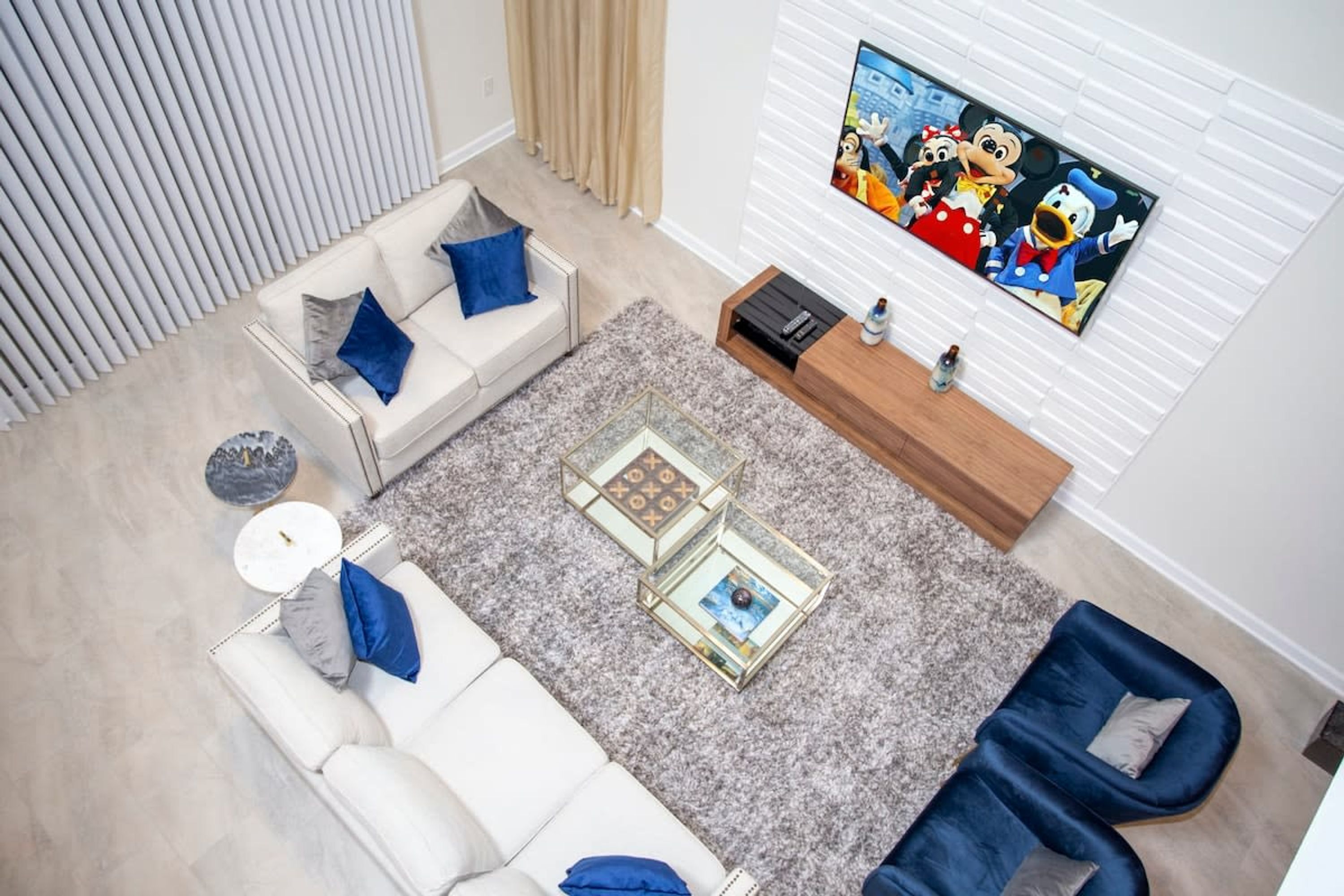 A modern living room with a white sofa, blue armchairs, a glass coffee table, and a flat-screen TV on the wall.