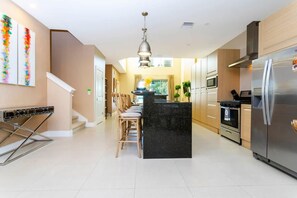 Una cocina moderna con una isla central, electrodomésticos de acero inoxidable y una escalera que conduce a otro nivel.