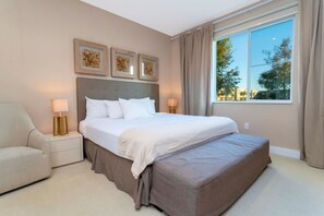 Una habitación de hotel con cama, mesitas de noche, una silla y un amplio ventanal con cortinas.