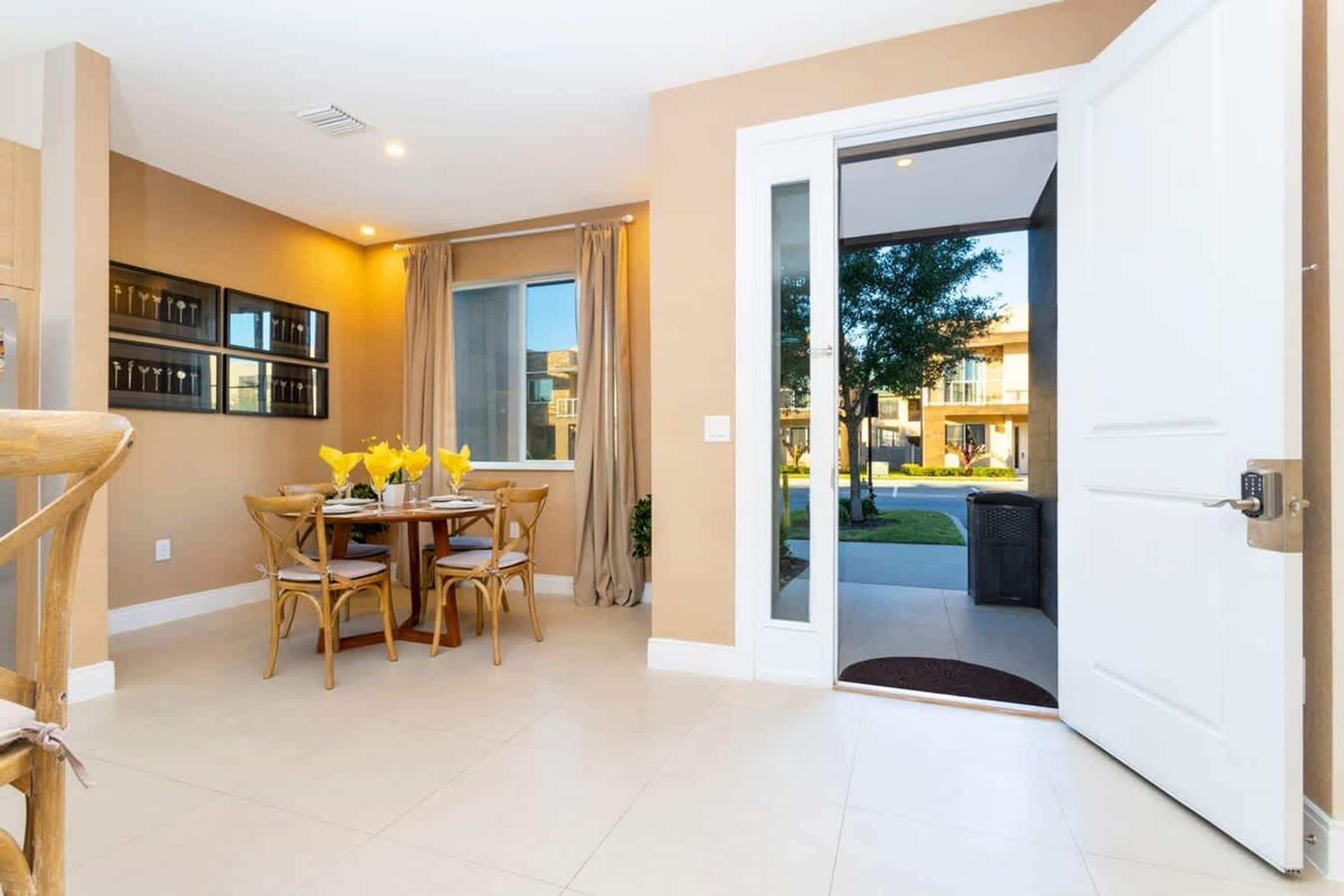 Una habitación con una mesa de comedor, sillas, una ventana con cortinas y una puerta que da al exterior.