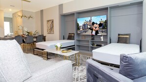Une chambre d’hôtel moderne équipée d’un téléviseur diffusant un dessin animé, d’un canapé, d’un lit, d’un coin repas avec des chaises et d’une petite table agrémentée d’objets décoratifs.