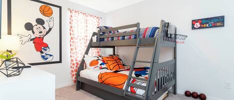 Una cama litera con temática de baloncesto, un cuadro con un personaje de caricatura y un letrero motivacional en la pared.