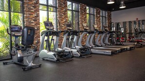 Une salle de sport équipée de plusieurs tapis de course et de plusieurs appareils elliptiques, de grandes fenêtres donnant sur un mur en briques et de divers appareils d’exercice.