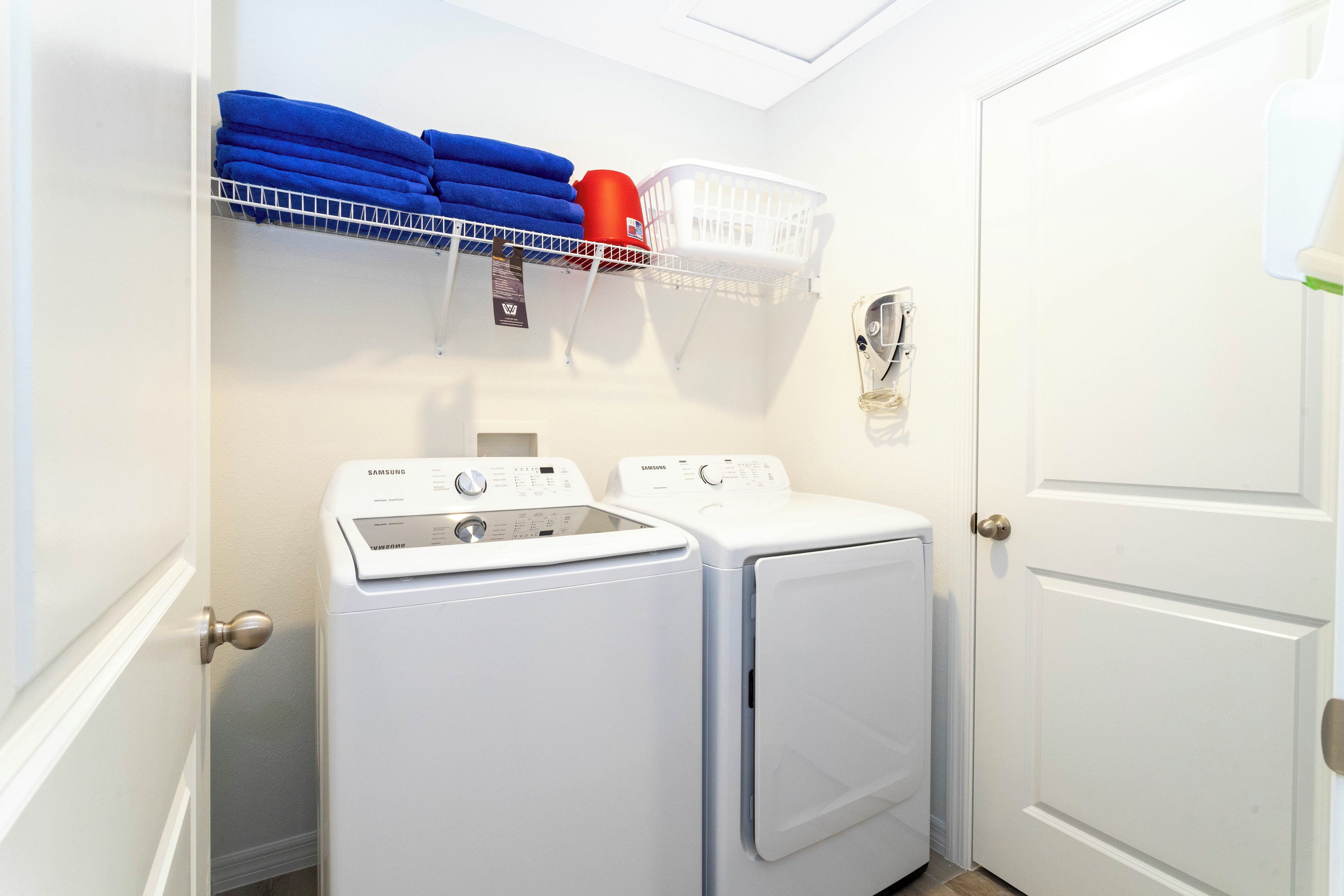 A laundry area with two white washing machines, a white basket, and blue towels on a shelf.