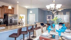 A modern kitchen with a central island, bar stools, and a dining area with a glass table set for six. - 5 Bedroom at Storey Lake Orlando FL Close to Disney 4851 (Kissimmee)