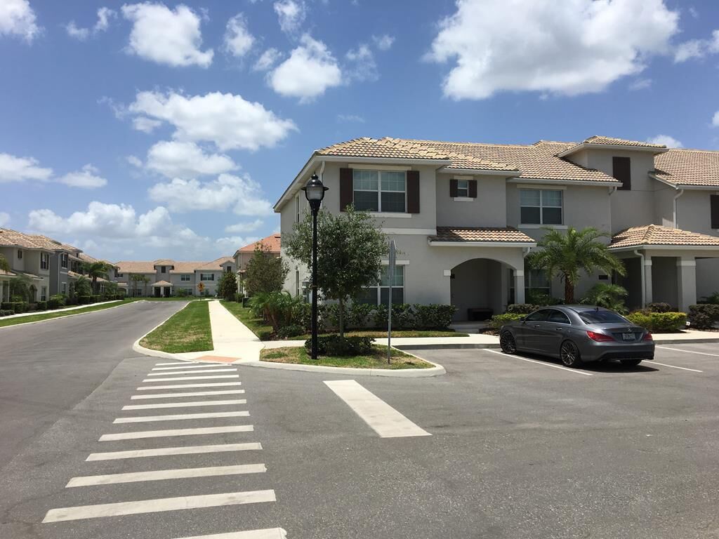 A residential street with a crosswalk, parked cars, and houses with tiled roofs.