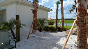 A beach area with a hammock, palm trees, a chair, and a building with a sign. - 5 Bedroom at Storey Lake Orlando FL Close to Disney 4851 (Kissimmee)