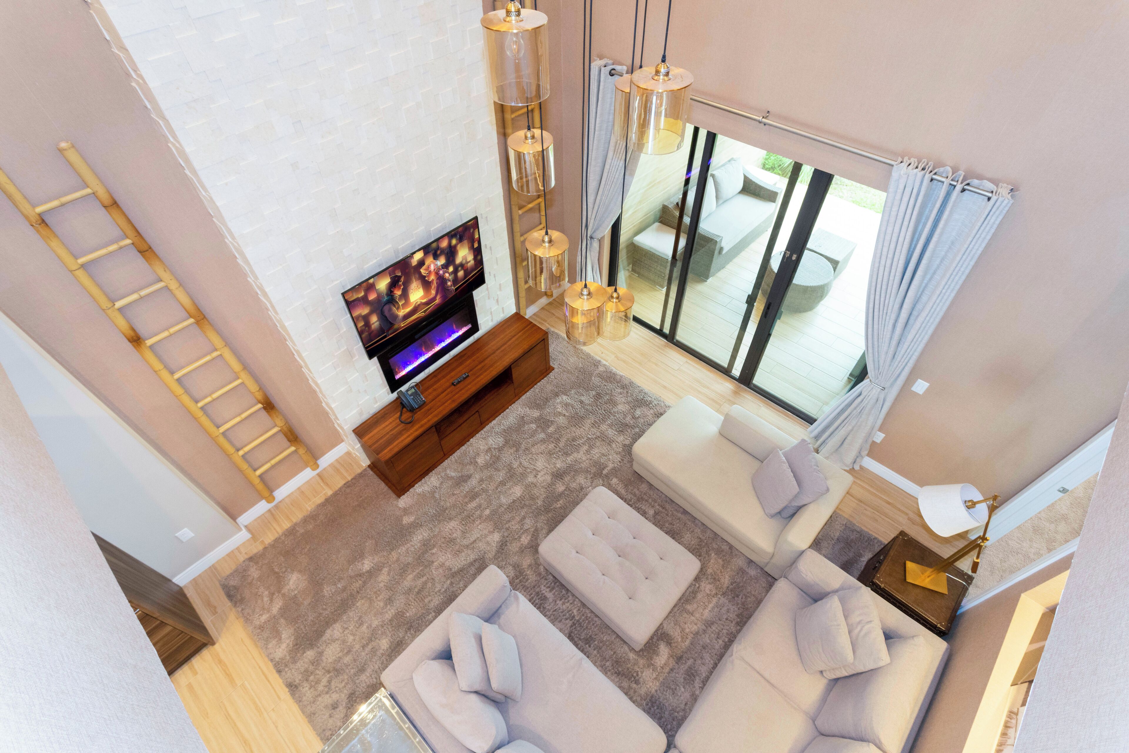 A modern living room with a flat-screen TV, a wooden ladder, a large window with curtains, and a sofa set.
