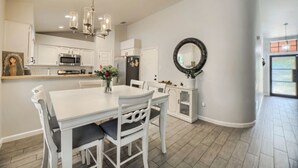Une cuisine moderne avec des meubles blancs, une table à manger avec des chaises, un lustre et un grand miroir au mur.