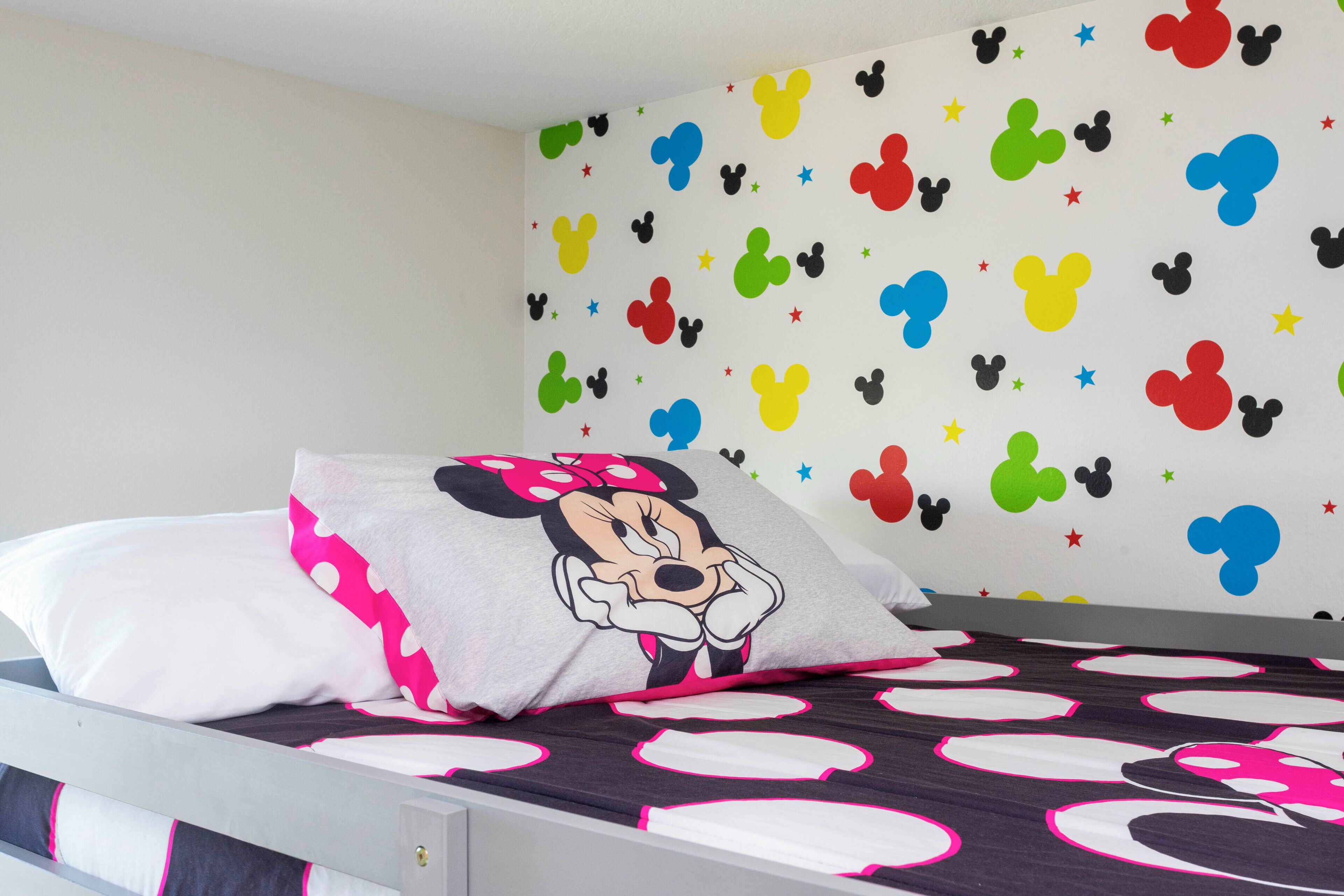 A bed with a Mickey Mouse pillow and a wall with colorful Mickey Mouse and star decals.