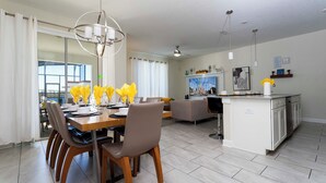 Une cuisine moderne avec des meubles blancs, un îlot central et un coin repas comprenant une table et des chaises en bois.