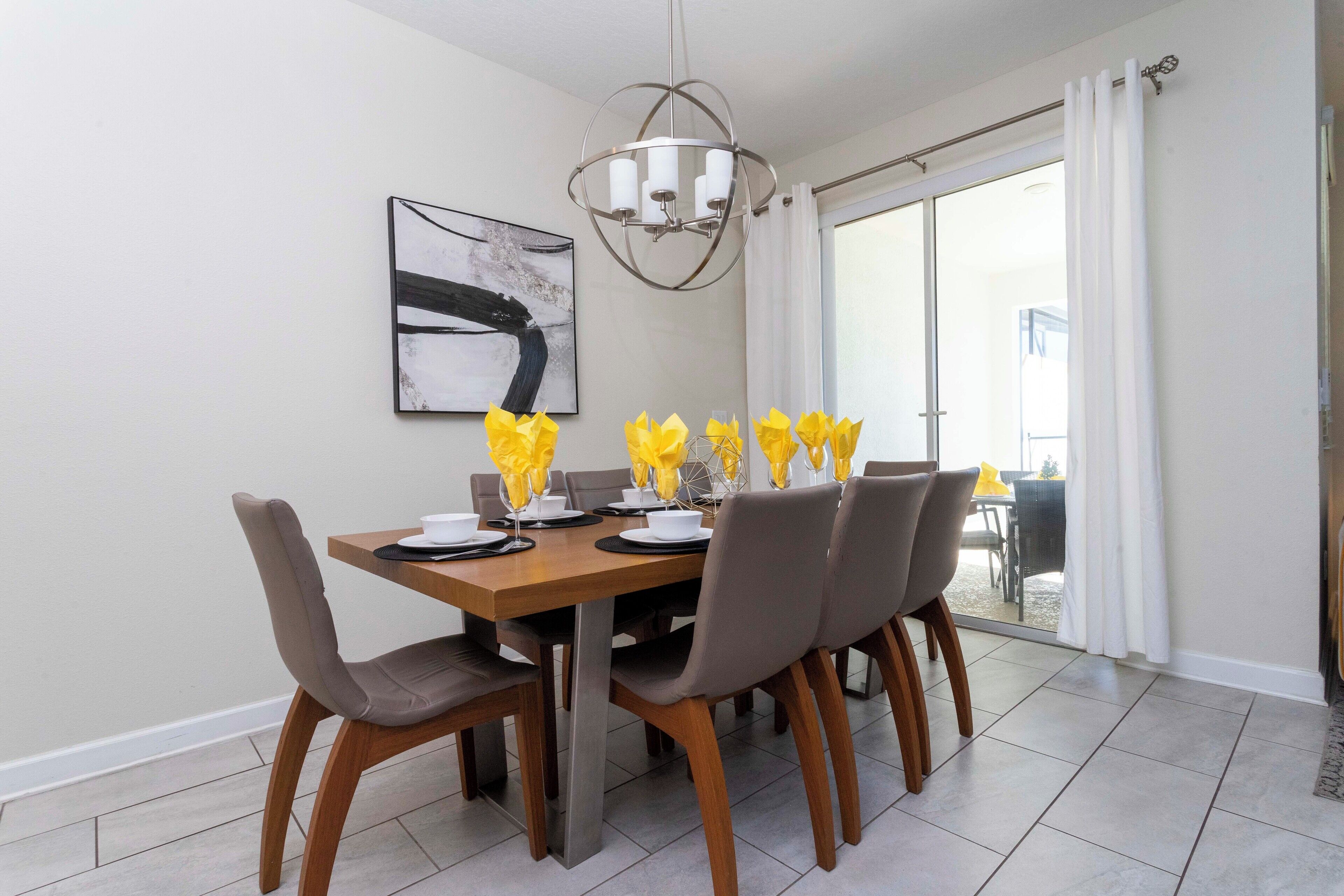 A dining area with a wooden table, grey chairs, and a modern chandelier.