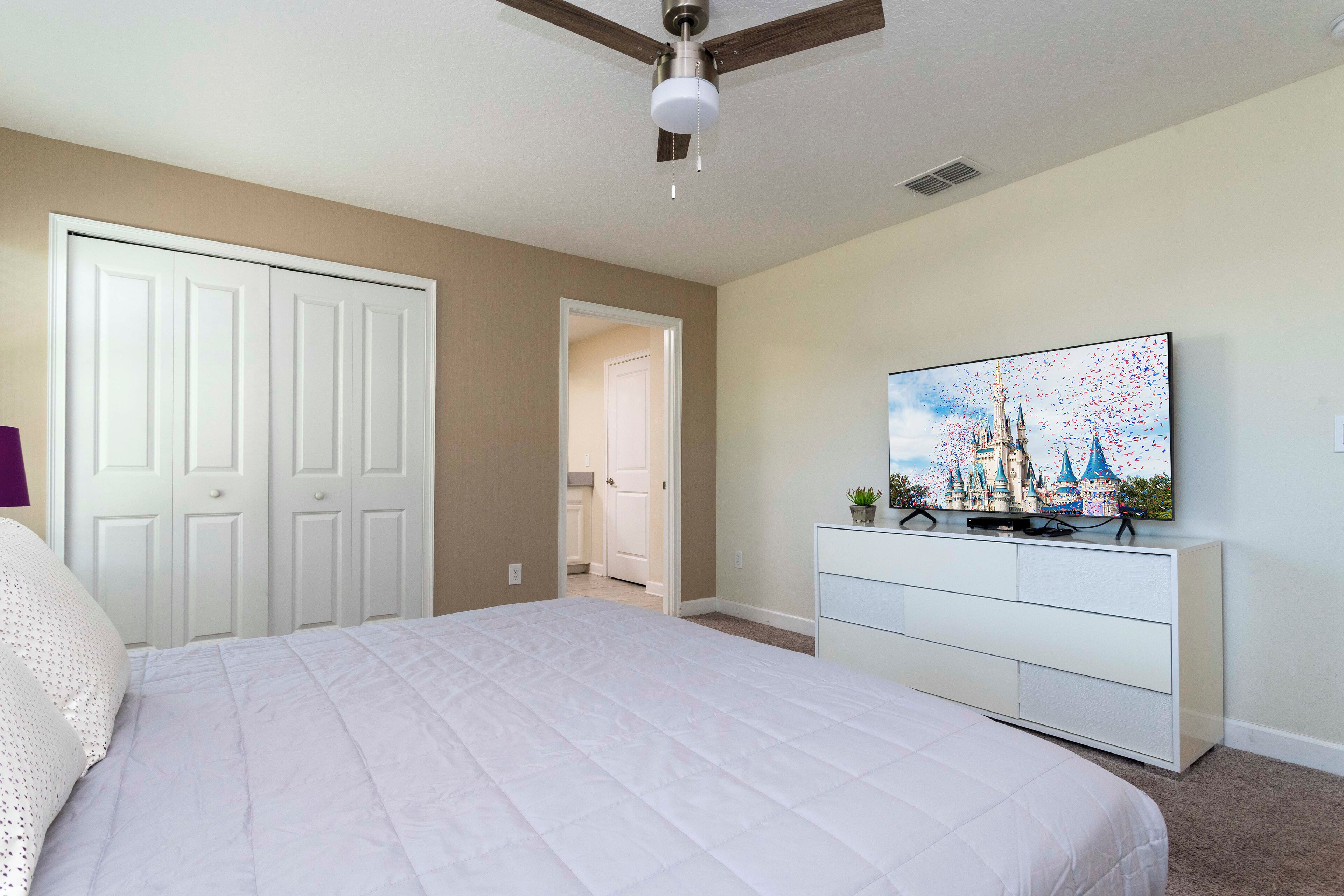 A bedroom with a bed, a dresser, a ceiling fan, and a wall-mounted TV.