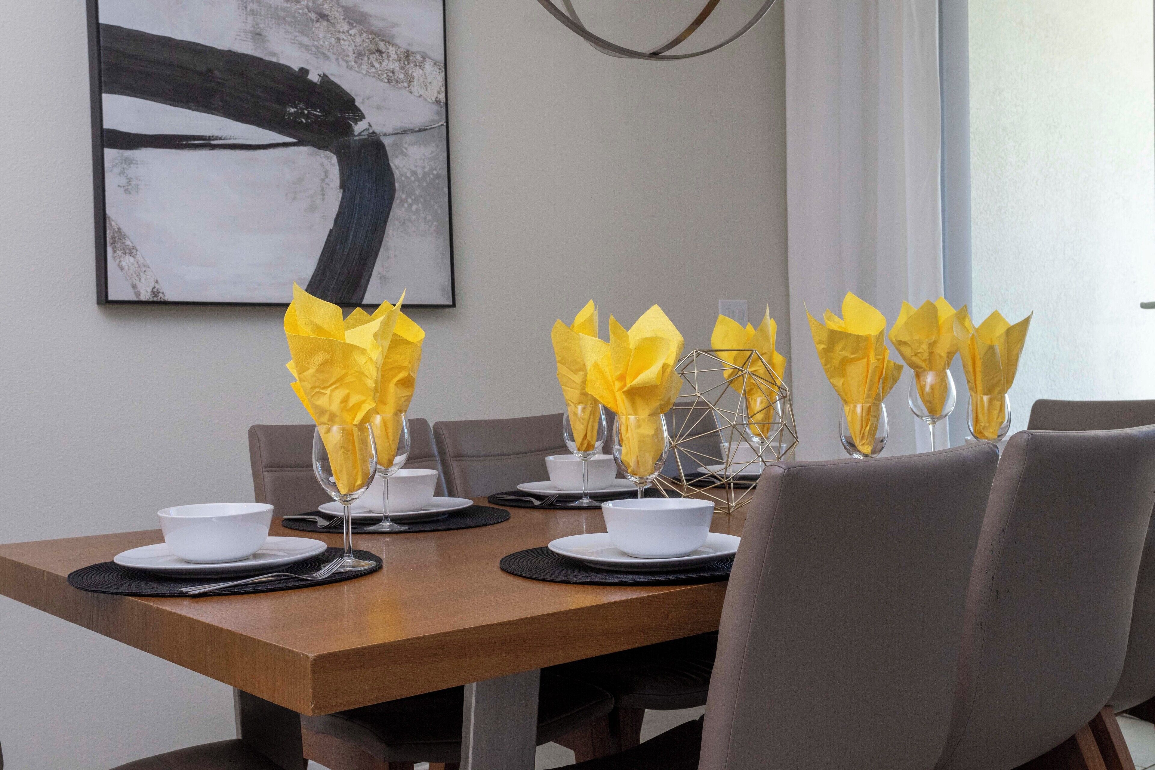 A dining table set with white bowls, wine glasses, and yellow napkins.