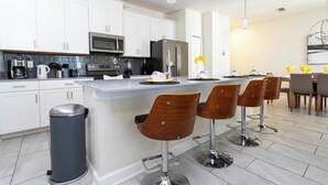 Une cuisine moderne avec des meubles blancs, des appareils en acier inoxydable et un îlot central doté de tabourets de bar.