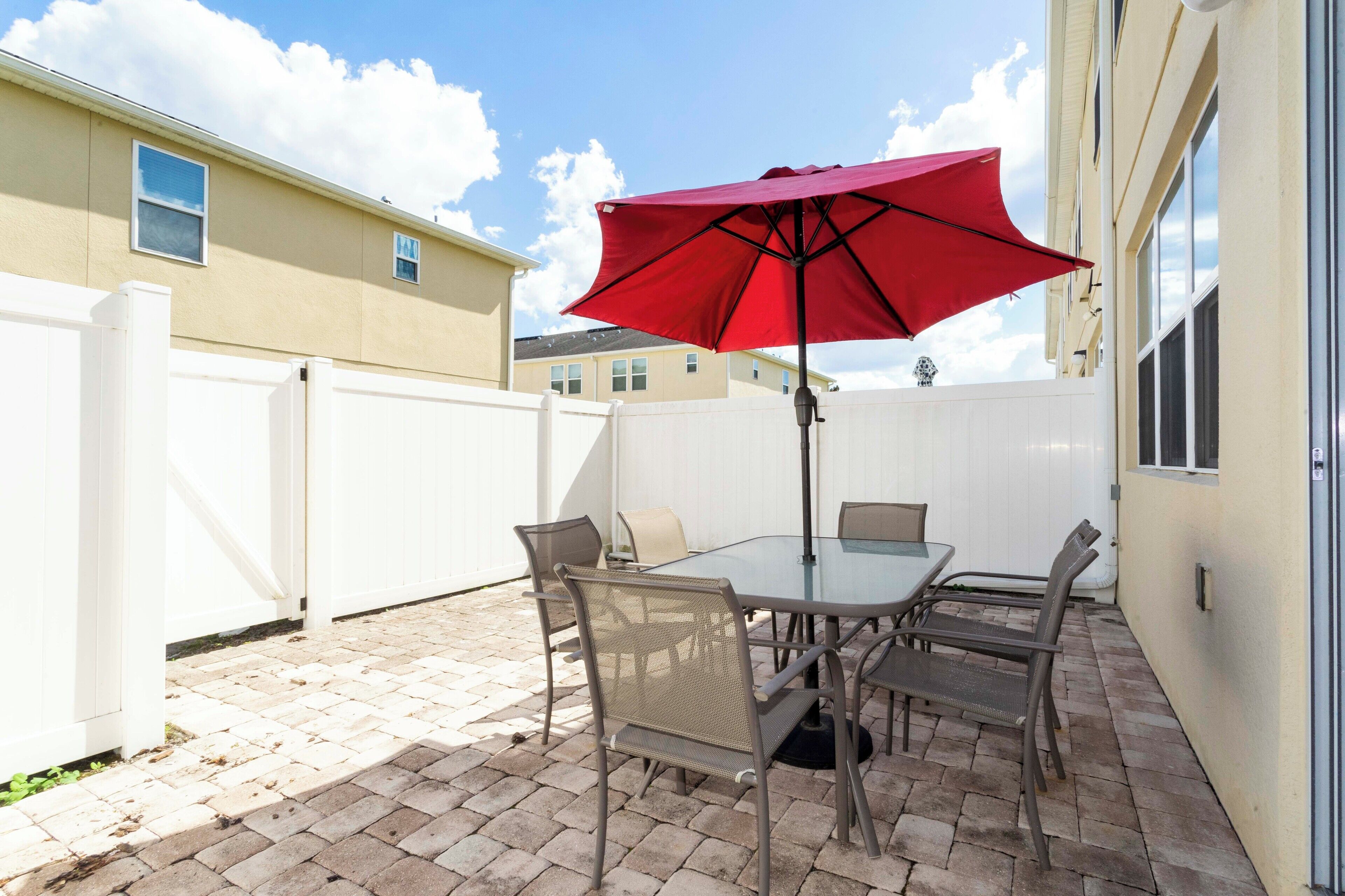 Une terrasse avec une table et des chaises, un parasol rouge et une clôture blanche.