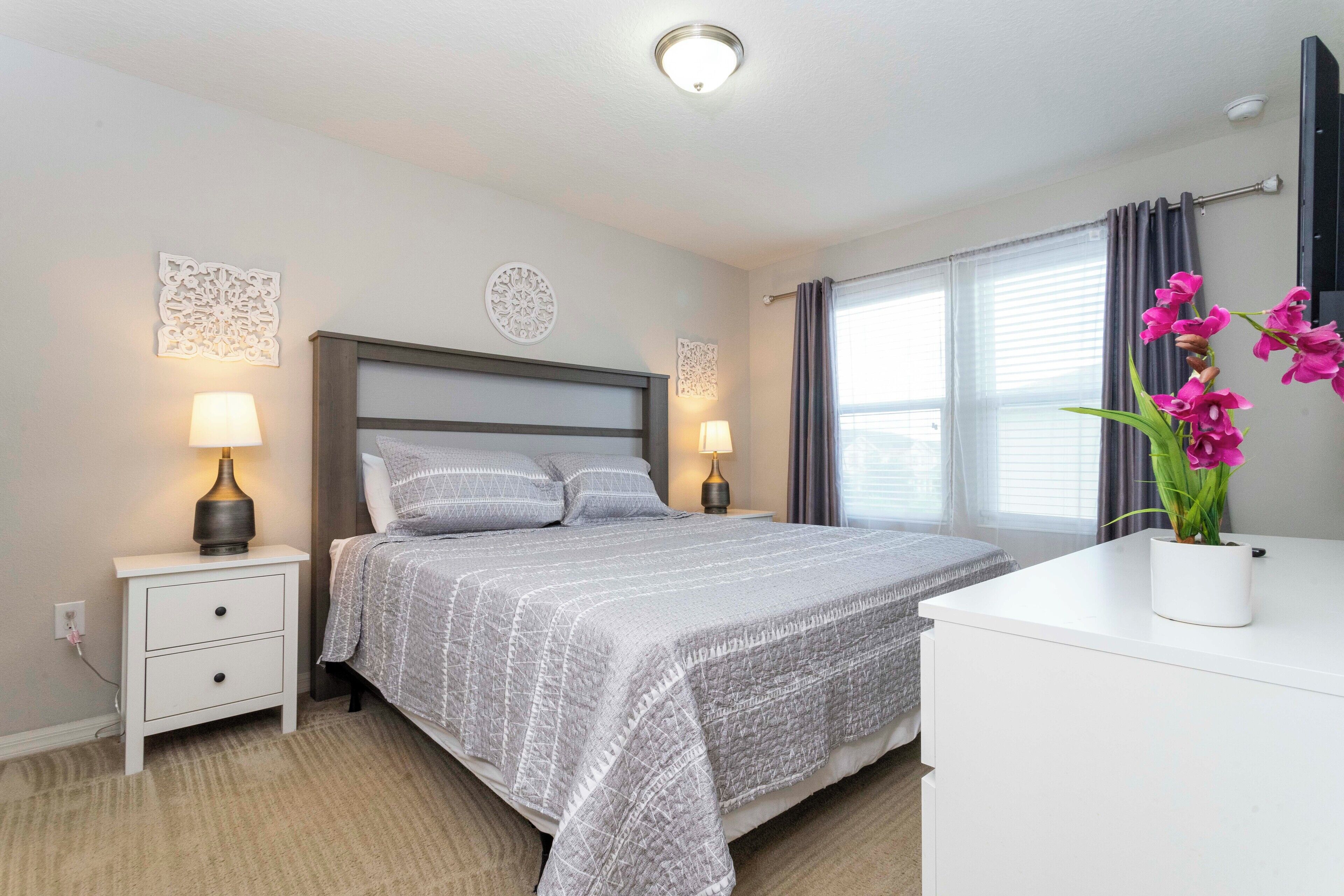 A neatly arranged bedroom with a bed, bedside tables with lamps, a dresser, and a window with curtains.
