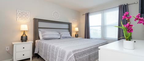 A neatly arranged bedroom with a bed, bedside tables with lamps, a dresser, and a window with curtains.