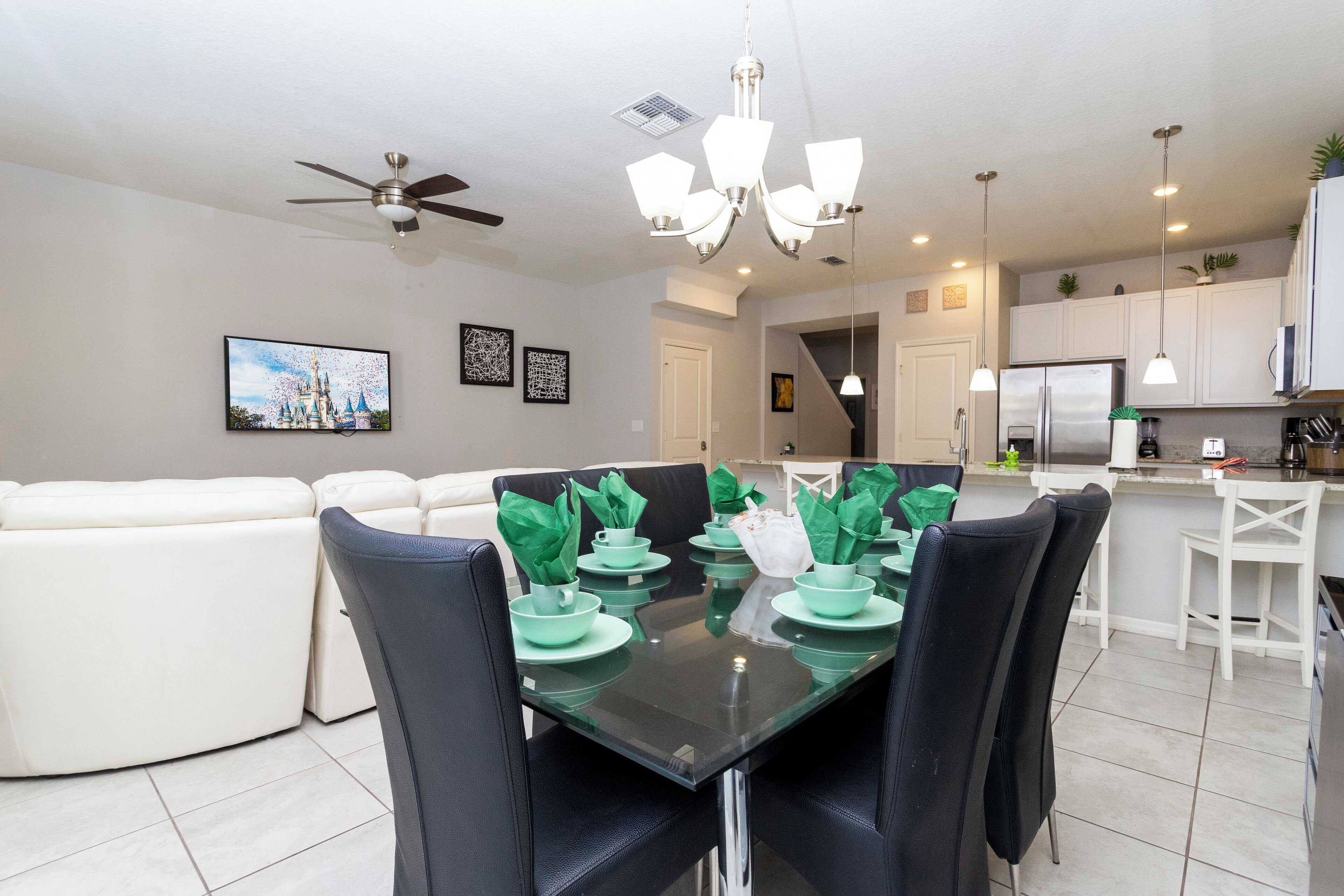 A modern kitchen with white cabinets, a stainless steel refrigerator, and a dining area with a glass table and black chairs.