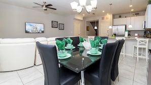 A modern kitchen with white cabinets, a stainless steel refrigerator, and a dining area with a glass table and black chairs. - Four Bedrooms Townhome Close to Disney 5162a (Kissimmee)