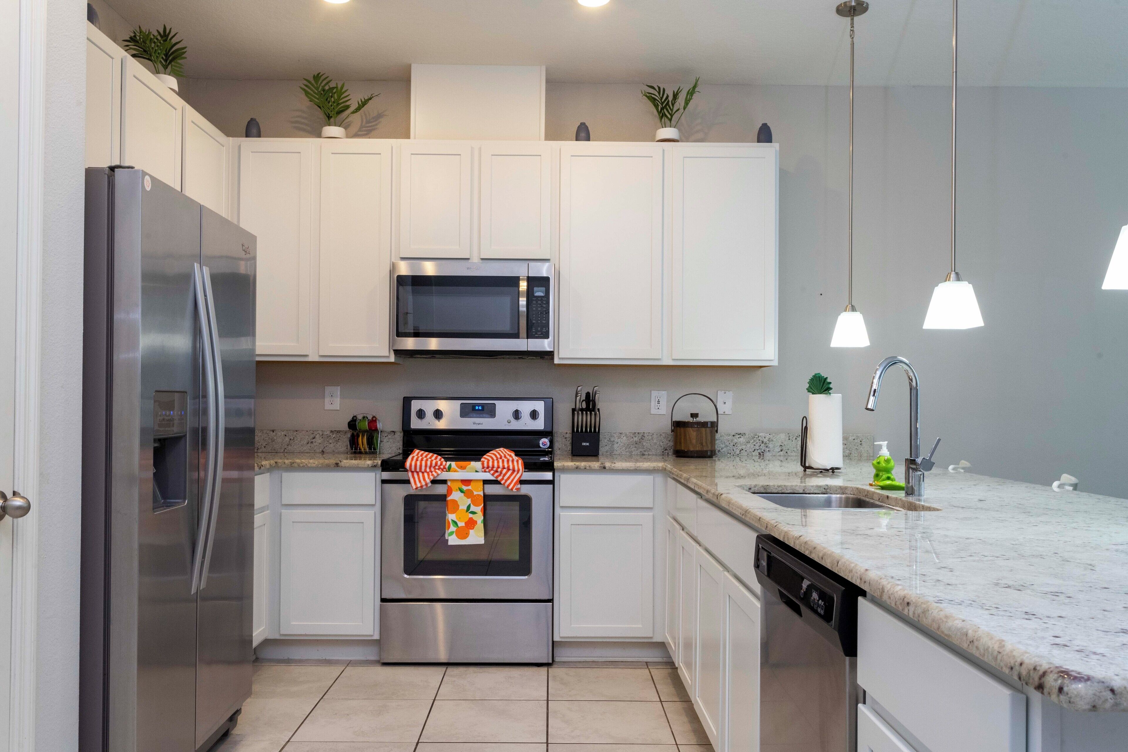 A modern kitchen with white cabinets, stainless steel appliances, a granite countertop, and pendant lighting.