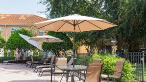 An outdoor patio with tables and chairs, surrounded by greenery and a building with a tiled roof. - Four Bedrooms Townhome Close to Disney 5162a (Kissimmee)