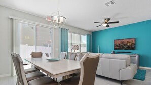 A modern living room with a dining area, a white sofa, teal walls, and a cityscape painting. - Wonderful 4 Bed Close to Disney w Gameroom 5150 (Kissimmee)