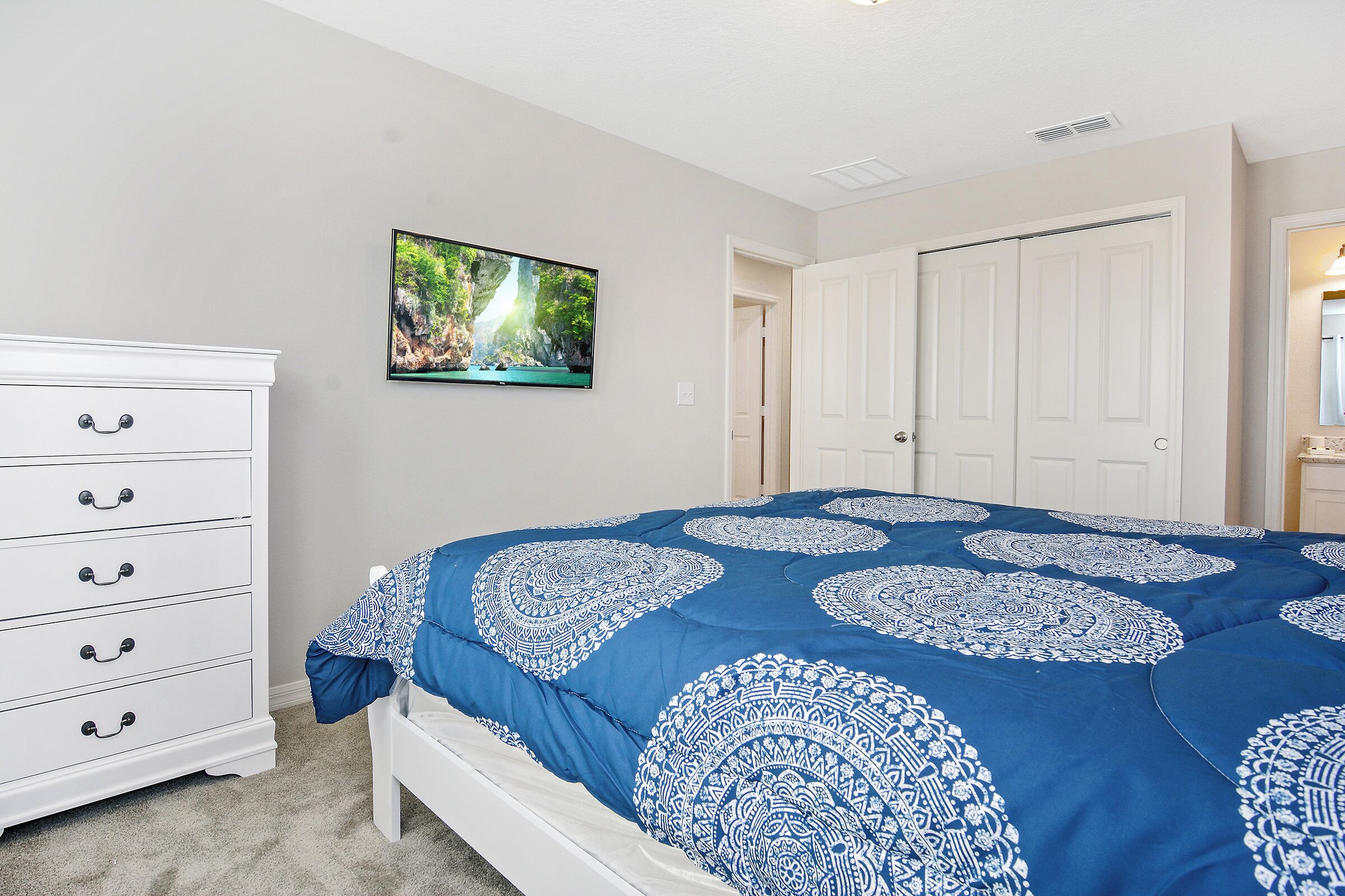 Ein Schlafzimmer mit Bett, Kommode, Fernseher und Tür.
