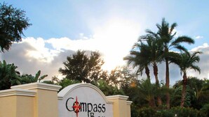Une enseigne pour Compass Bay, avec un logo en forme de boussole, entourée de palmiers et sous un ciel dégagé.