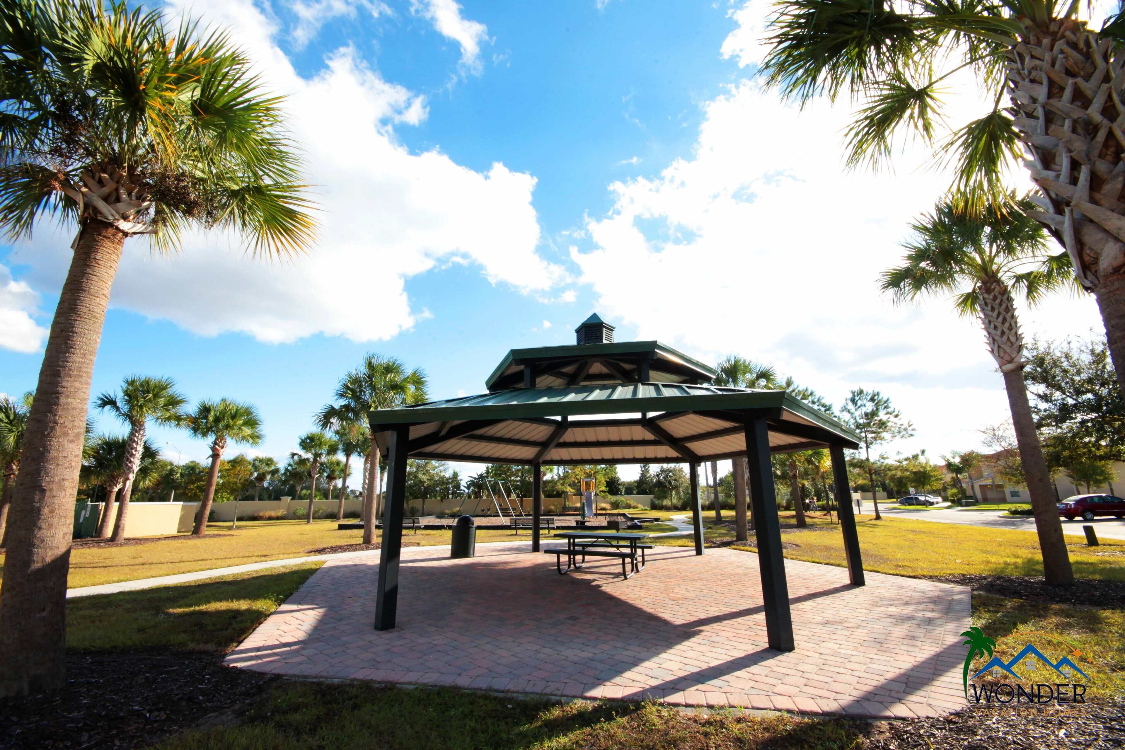 A gazebo with a roof, surrounded by palm trees and a brick pathway.