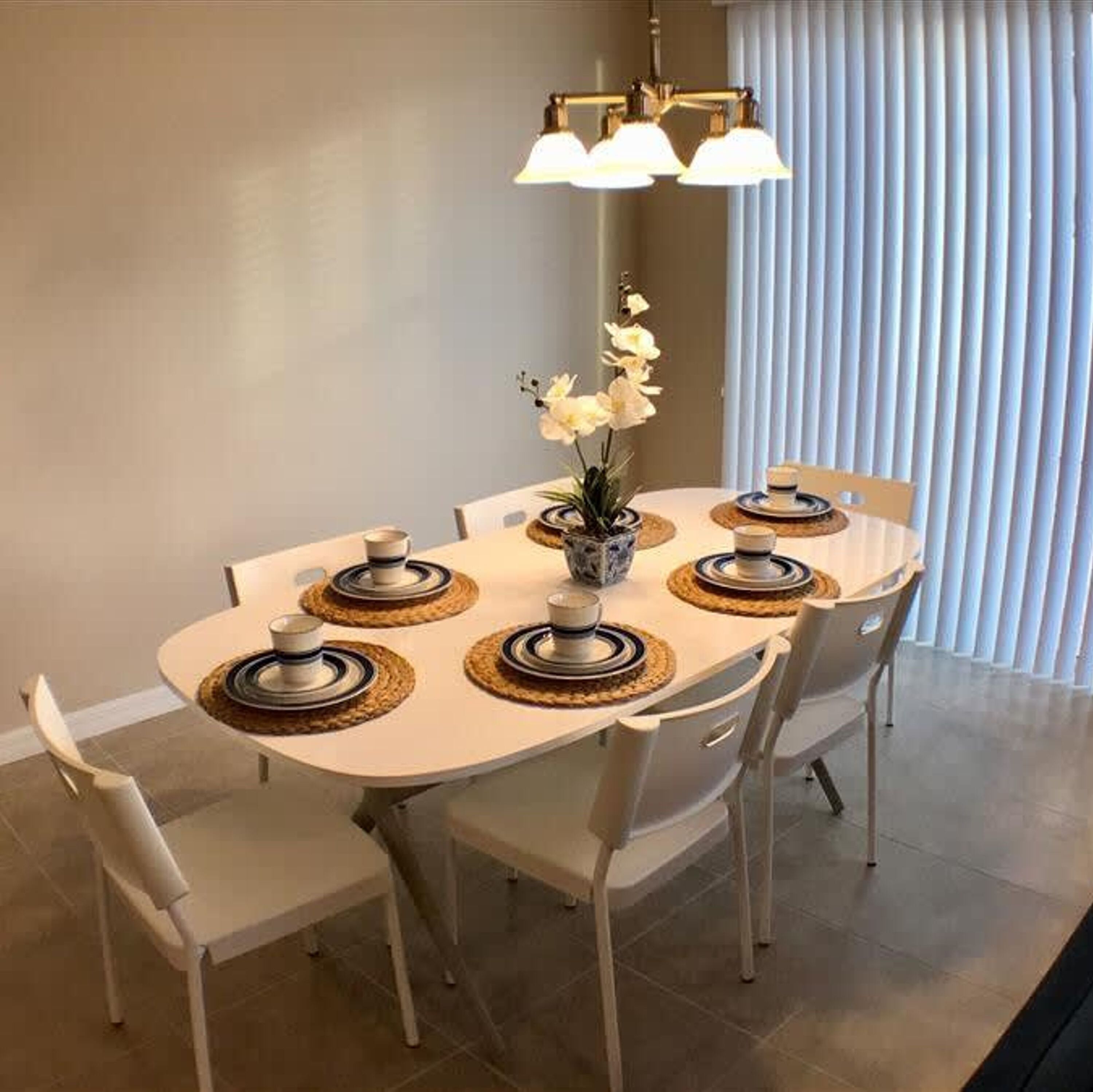 A dining area with a round table, white chairs, and a vase with white flowers.