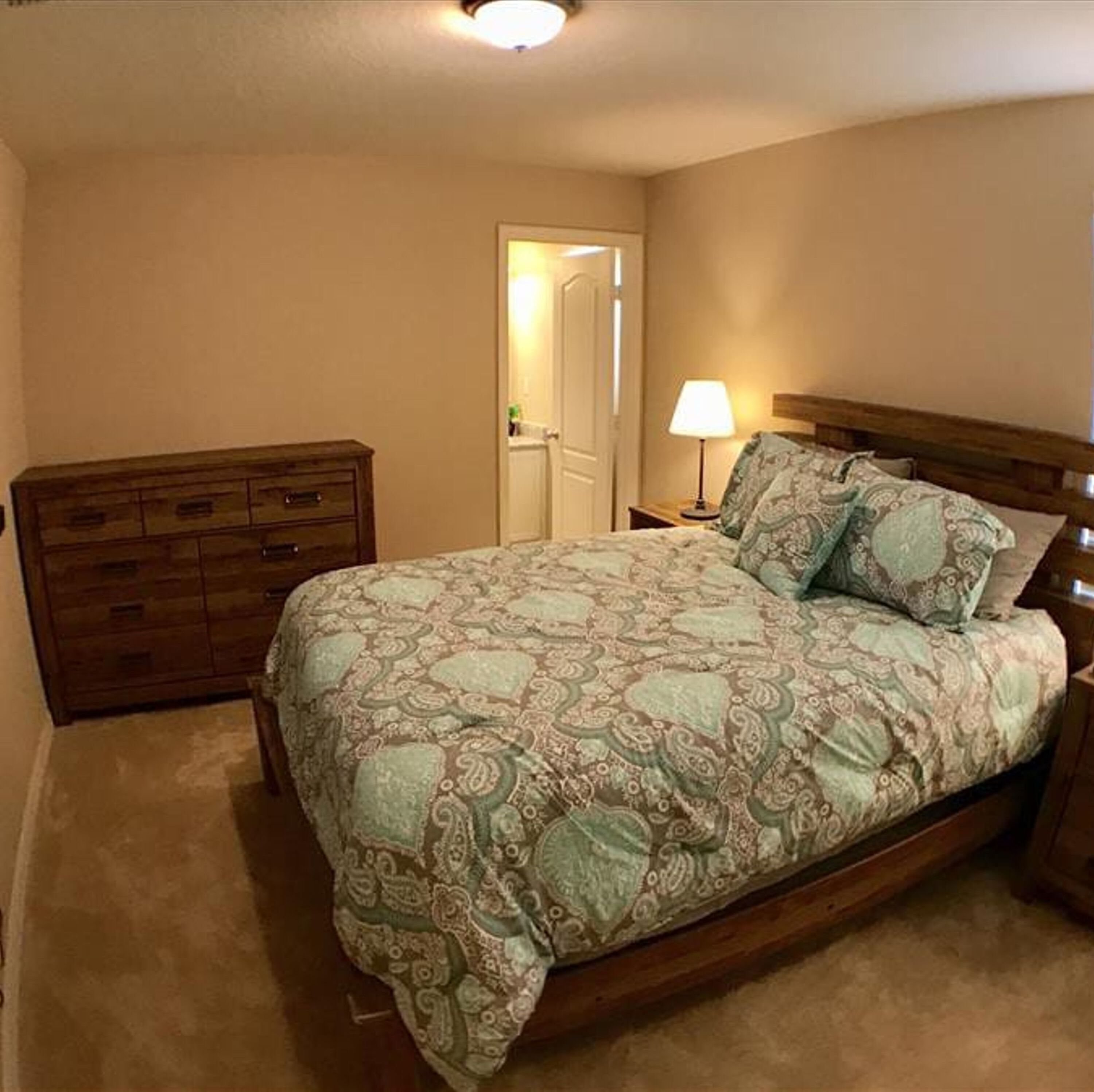 Une chambre à coucher avec un lit, une commode en bois et une table de chevet avec une lampe.