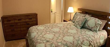 Une chambre à coucher avec un lit, une commode en bois et une table de chevet avec une lampe.