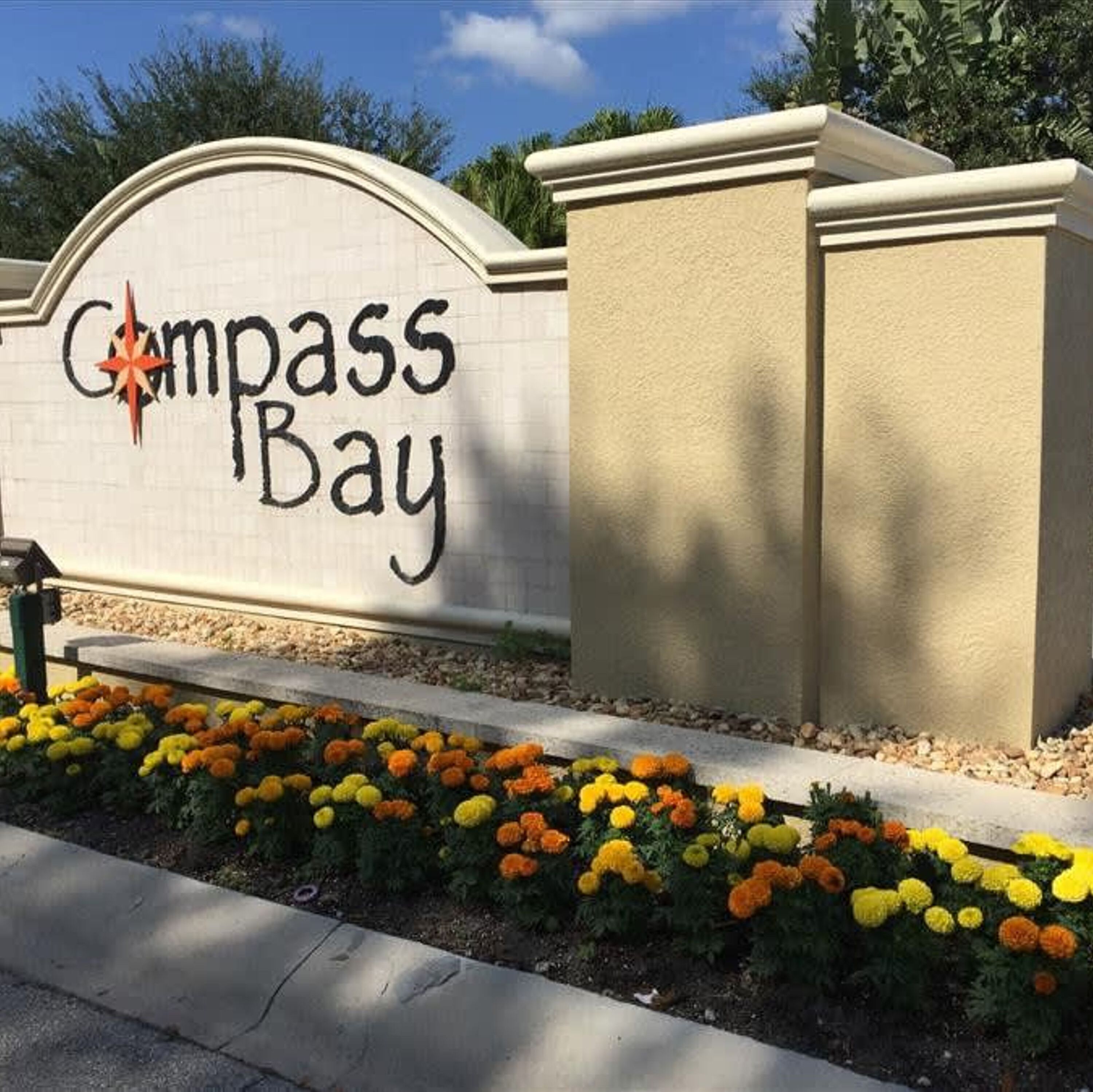 A sign for Compass Bay with a decorative star and a flower bed in front.