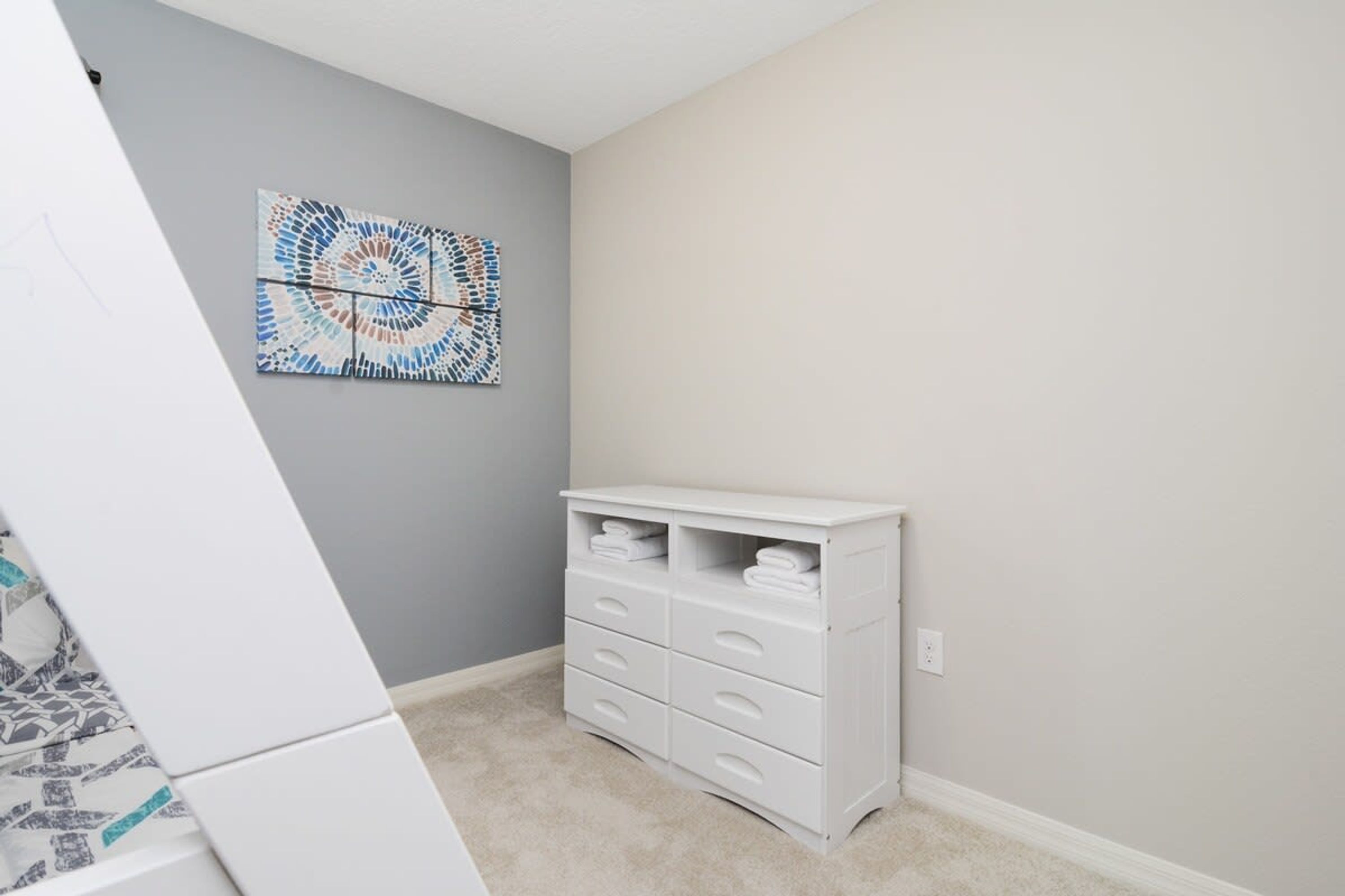Une pièce avec un mur gris, une commode blanche à tiroirs et un tableau abstrait aux couleurs bleue et blanche.