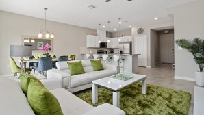 Een moderne woonkamer met een witte bank, groene kussens, een salontafel en een eethoek met stoelen en een tafel.