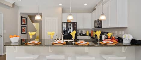 A modern kitchen with a central island, bar stools, white cabinetry, and pendant lighting.