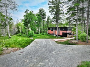A cabin with a gravel driveway, surrounded by dense forest. - Near Pictured Rocks and trails, on the AuTrain River, has private hot tub (Au Train)