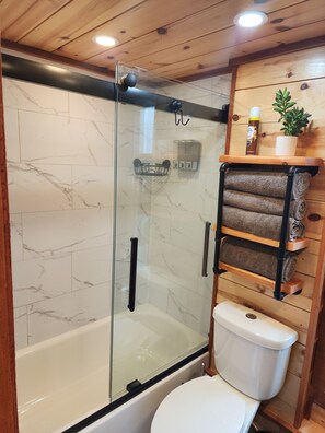 A bathroom with a glass-enclosed shower, a white toilet, and a wooden shelf with towels and toiletries. - Near Pictured Rocks and trails, on the AuTrain River, has private hot tub (Au Train)