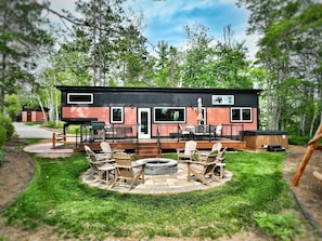 Relax on the spacious deck with Adirondack chairs and a fire pit, surrounded by lush greenery.