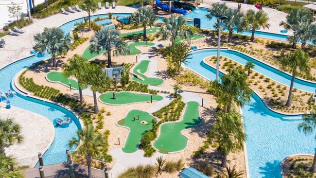 A golf course with a pool, palm trees, and a water slide. - Family Friendly Four Bd w Pool at Storey Lake Resort 5035 (Kissimmee)