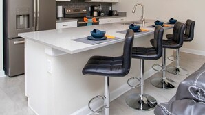 A modern kitchen with white cabinets, stainless steel appliances, and a central island with bar stools. - Family Friendly Four Bd w Pool at Storey Lake Resort 5035 (Kissimmee)