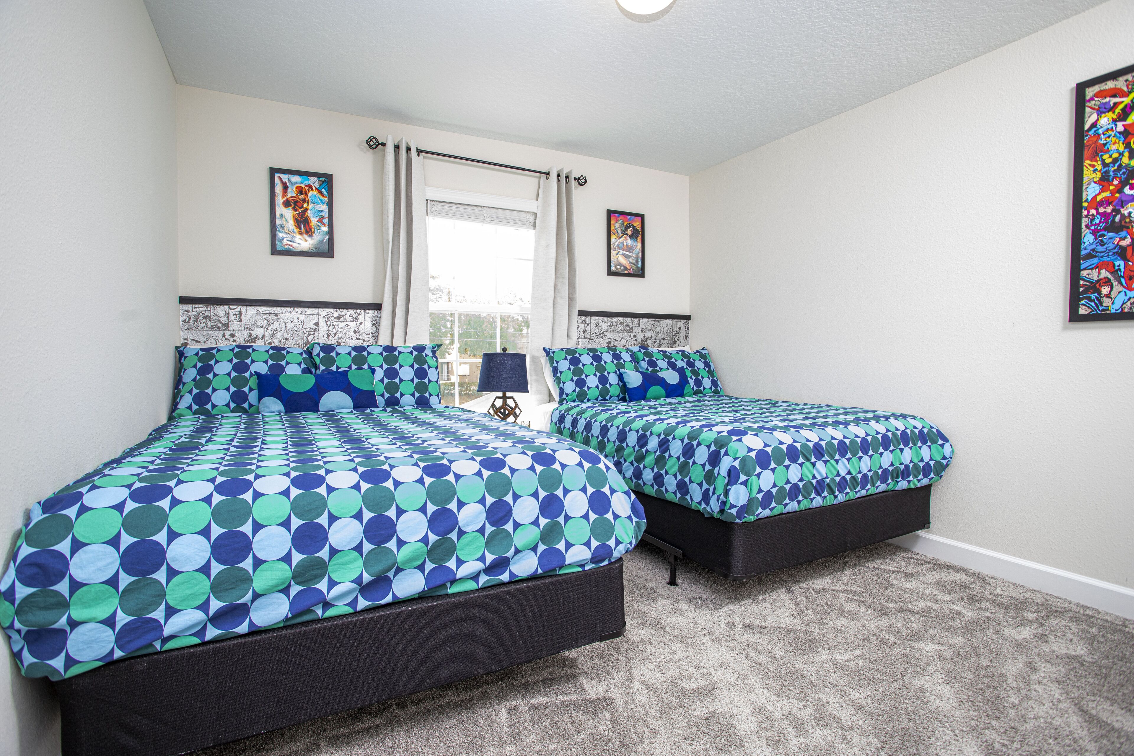 A bedroom with two beds, a window with curtains, and artwork on the walls.