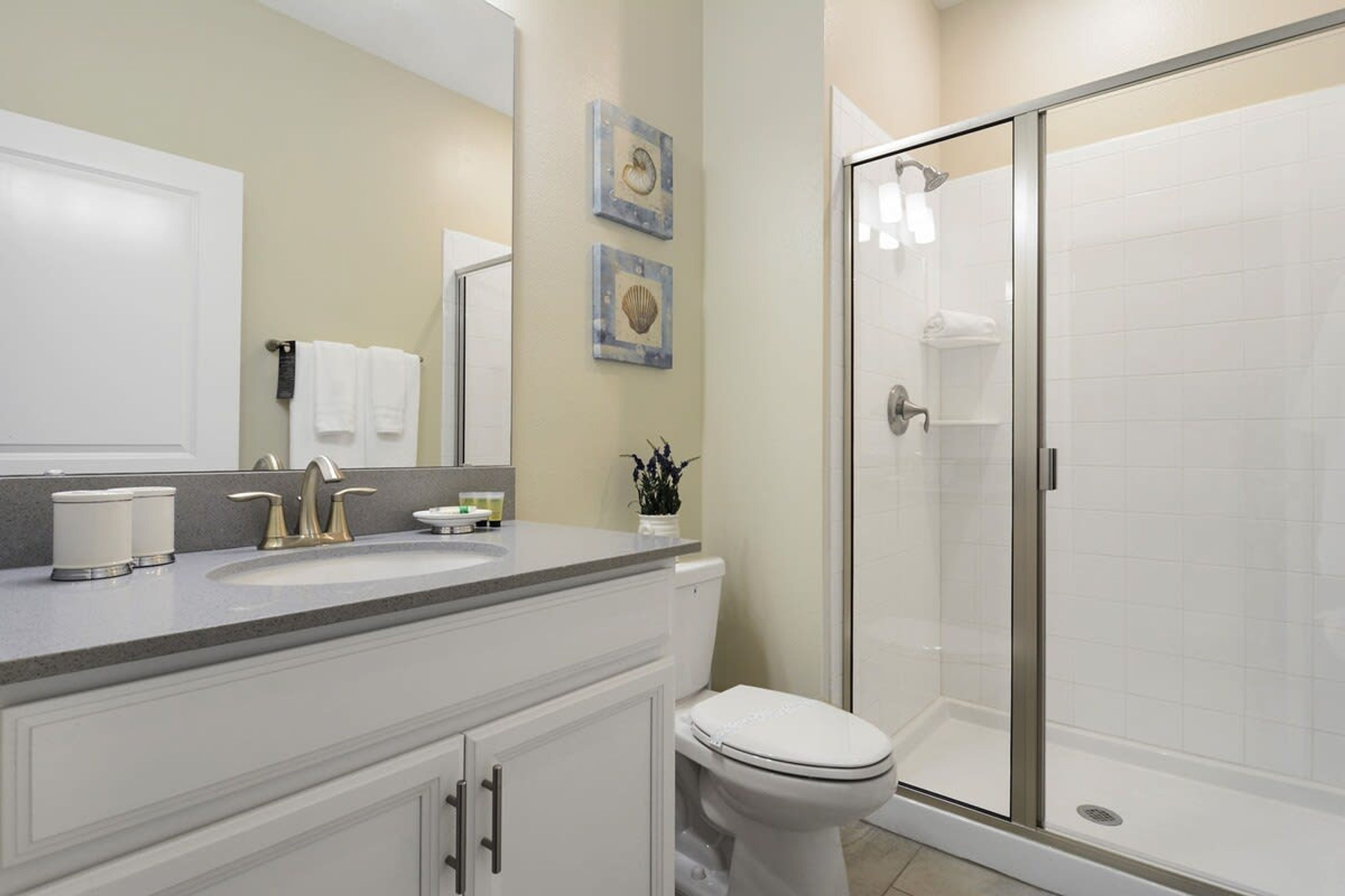 A bathroom with a shower, toilet, sink, and cabinets.