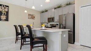 A modern kitchen with a central island, dark chairs, and stainless steel appliances. - Four Bedroom Close to Disney w Pool 4898 (Kissimmee)