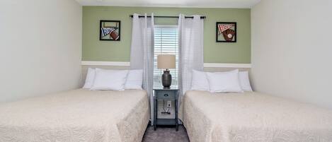 Une chambre d’hôtel avec deux lits simples, une table de chevet avec une lampe et une fenêtre avec des rideaux.